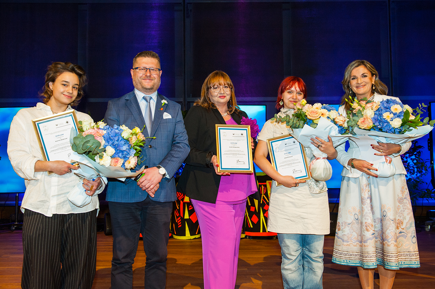 kilka osób na scenie z kwiatami i dyplomami