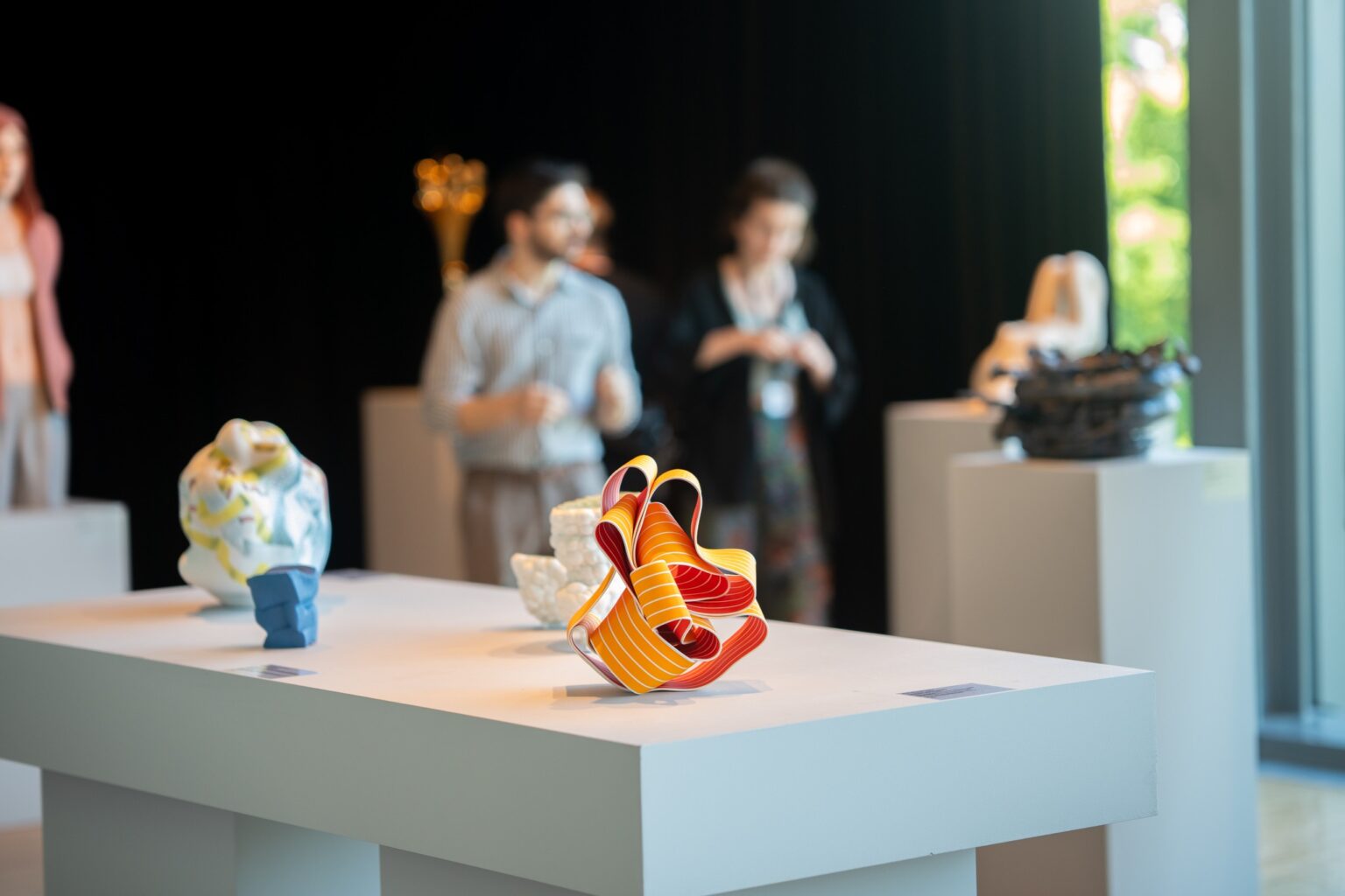 rzeżba ceramiczna w pomarańczowym kolorze, na drugim planie zwiedzający wystawę