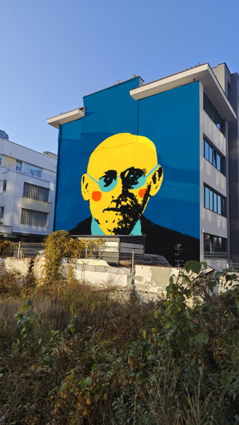 zewnętrzna ściana budynku z muralem w postaci rysunku w mocnych barwach przedstawiającego wizerunek mężczyzny w okularach pod krawatem