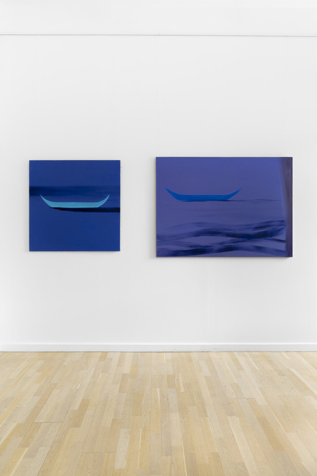 dwa obrazy na ścianie w przestrzeni wystawy przedstawiające łódki