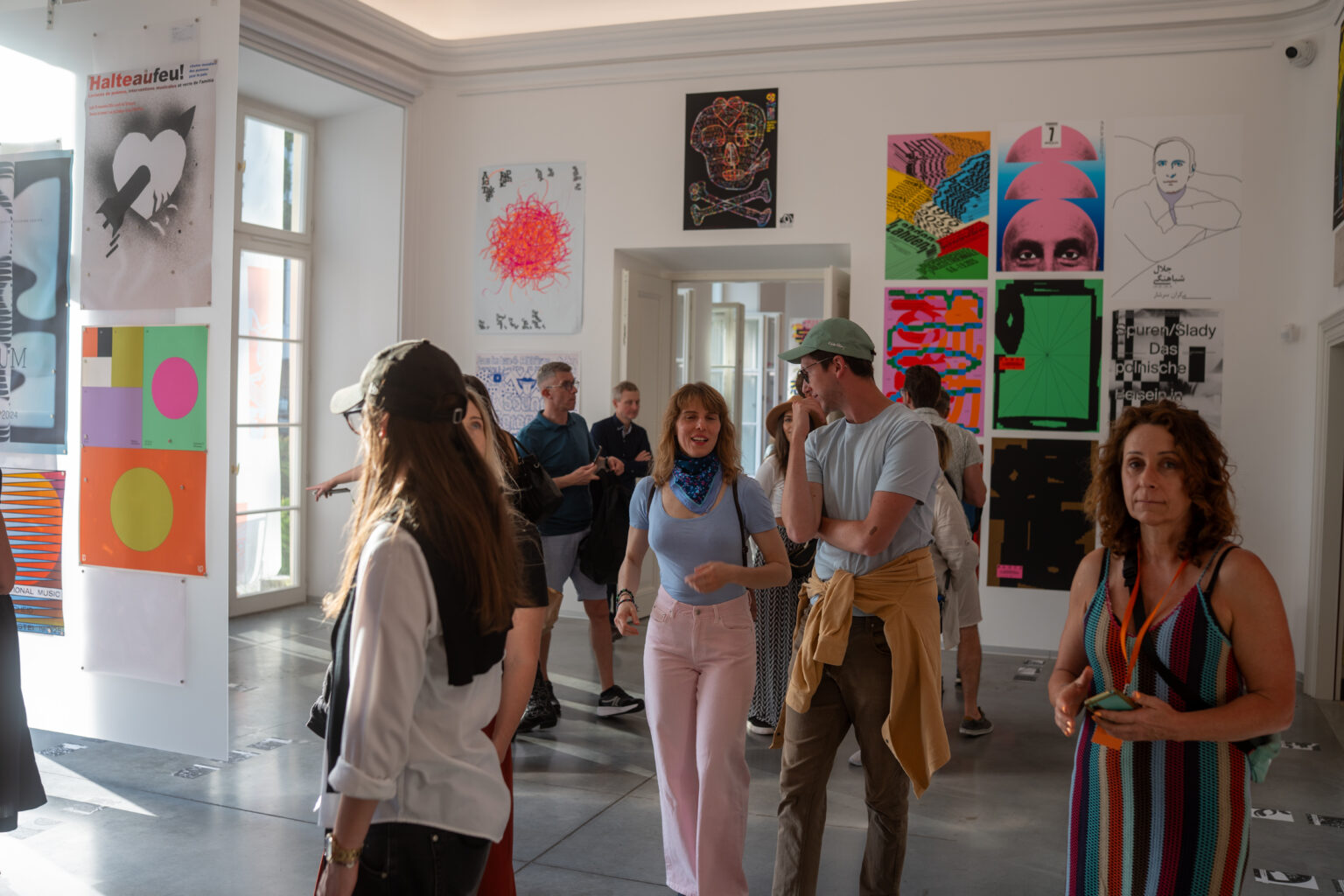 Ludzie oglądają dzieła sztuki. W tle widać plakaty i obrazy w różnych stylach i kolorach.