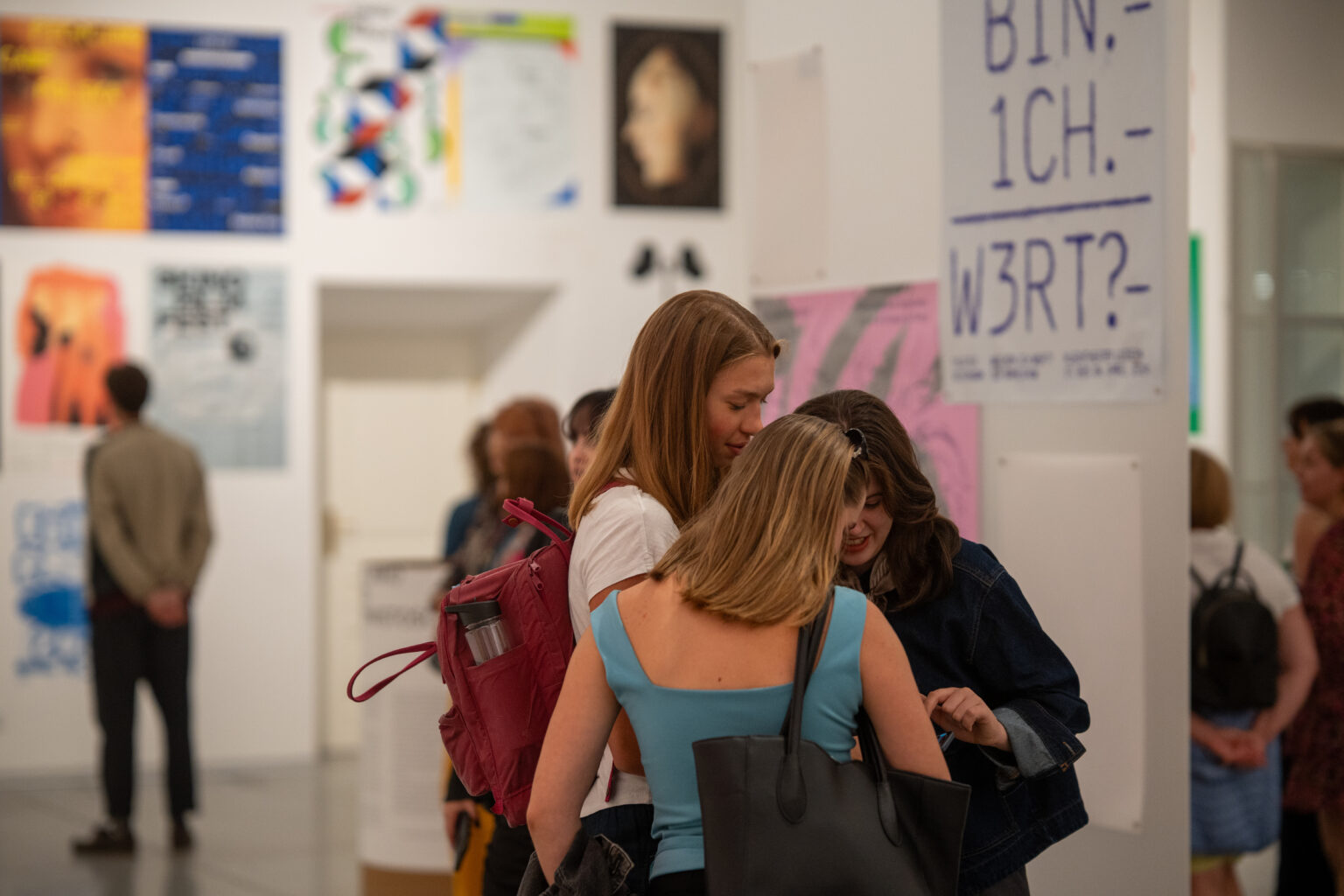 Ludzie oglądają dzieła sztuki. W tle widać plakaty w różnych stylach i kolorach.