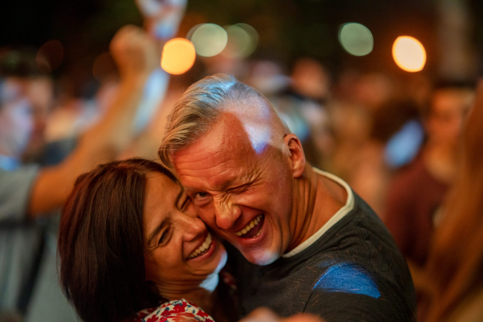 Szczęśliwa para na imprezie lub koncercie. Mężczyzna z siwymi włosami i uśmiechnięta kobieta przytulają się i pozują do zdjęcia.