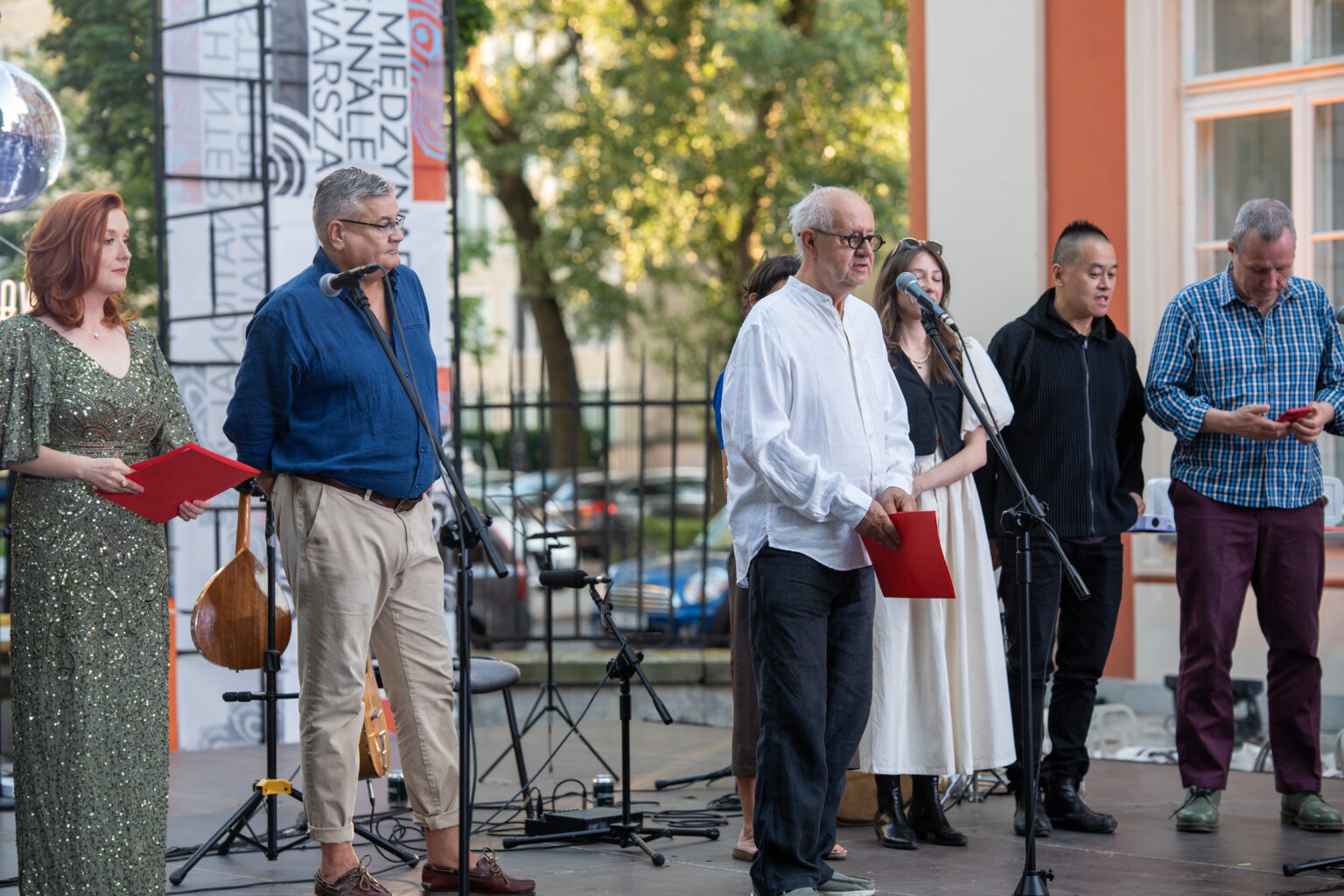 Grupa sześciu osób, w tym kobieta w cekinowej sukni i mężczyzna w białej koszuli, stoi na scenie podczas Międzynarodowego Biennale Plakatu.