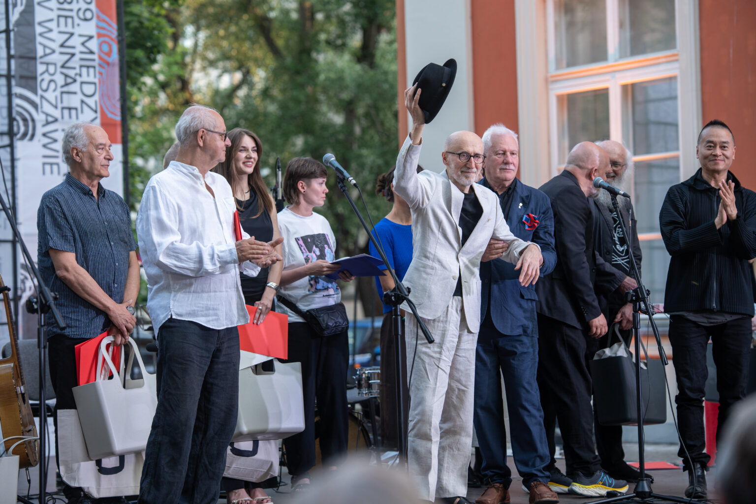Na scenie, podczas 29. Międzynarodowego Biennale Plakatu w Warszawie, zebrana jest grupa dorosłych, którzy uśmiechają się i biją brawa.