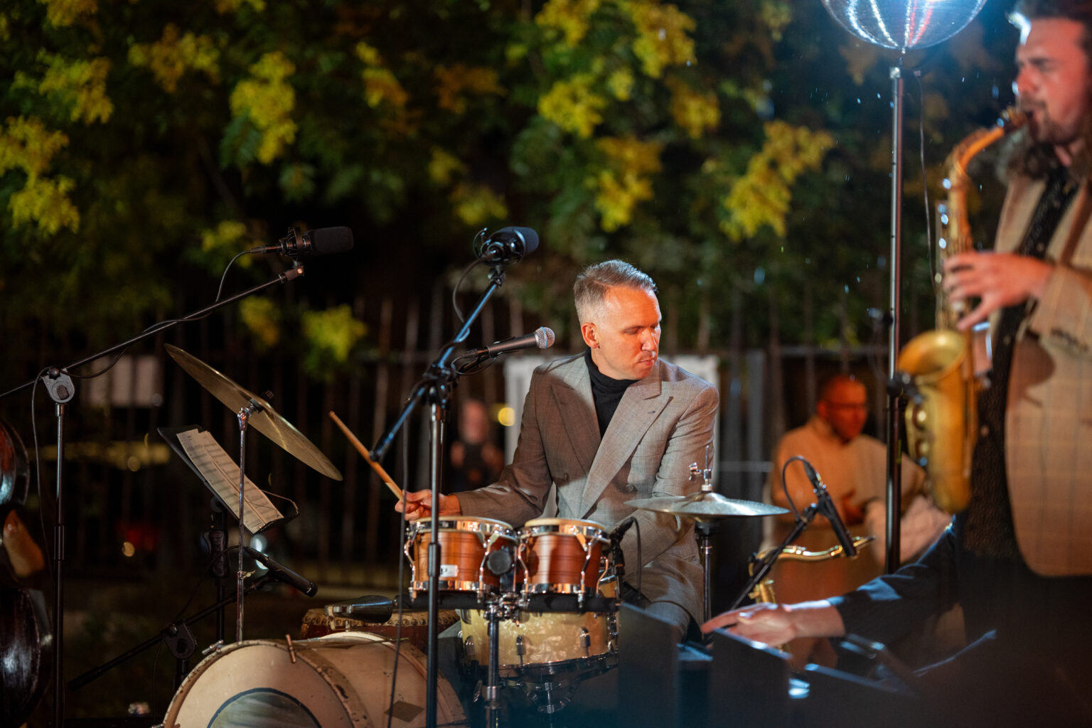 Mężczyzna gra na perkusji podczas występu na świeżym powietrzu. Po prawej stronie widać saksofonistę.