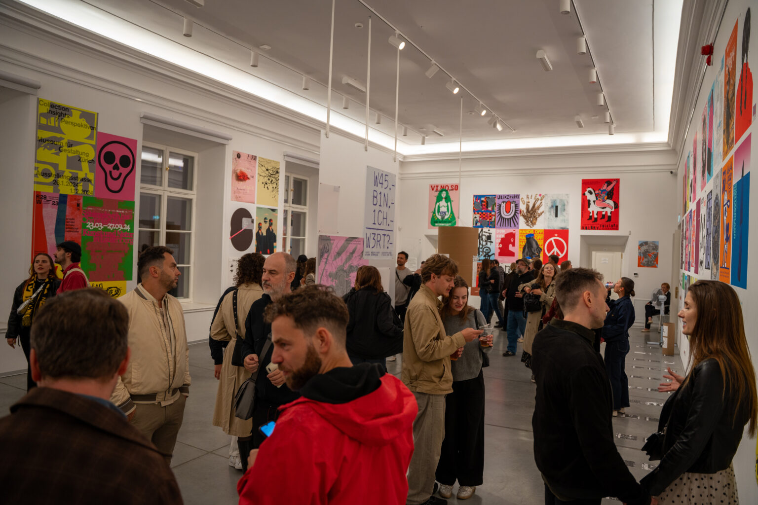 Ludzie oglądają wystawę sztuki. W tle widać plakaty i obrazy w różnych stylach i kolorach.