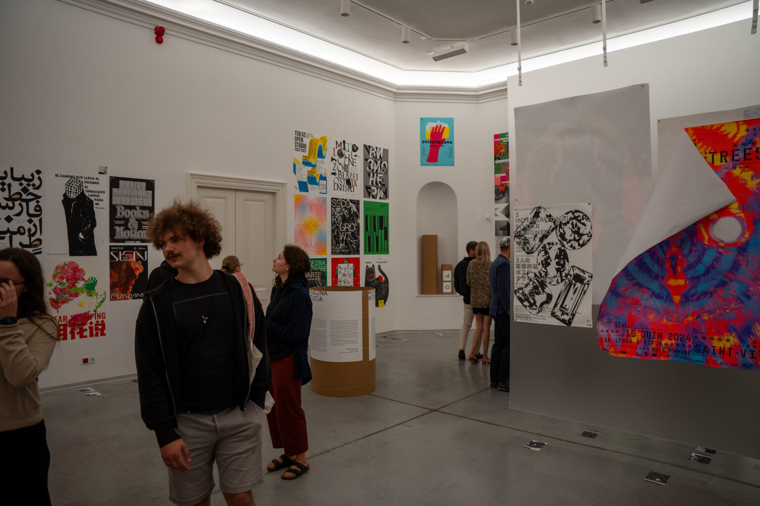 Ludzie oglądają wystawę sztuki. W tle widać plakaty w różnych stylach i kolorach.