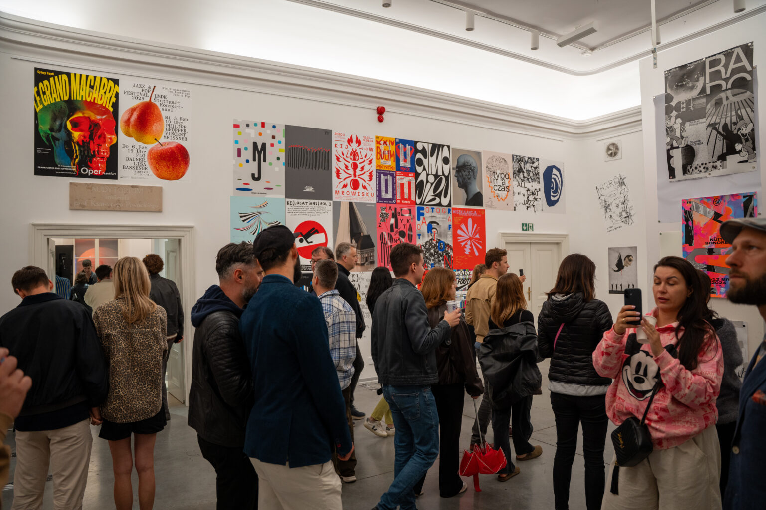 Ludzie oglądają wystawę sztuki. W tle widać plakaty w różnych stylach i kolorach.