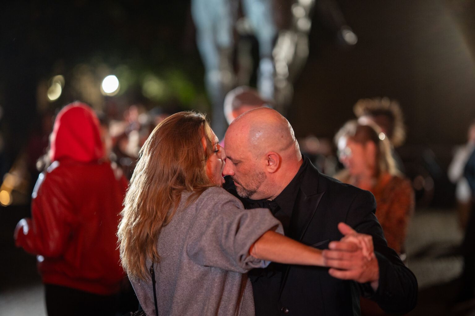 Mężczyzna i kobieta tańczą na zewnątrz w nocy, podczas imprezy. Ich twarze są blisko siebie.