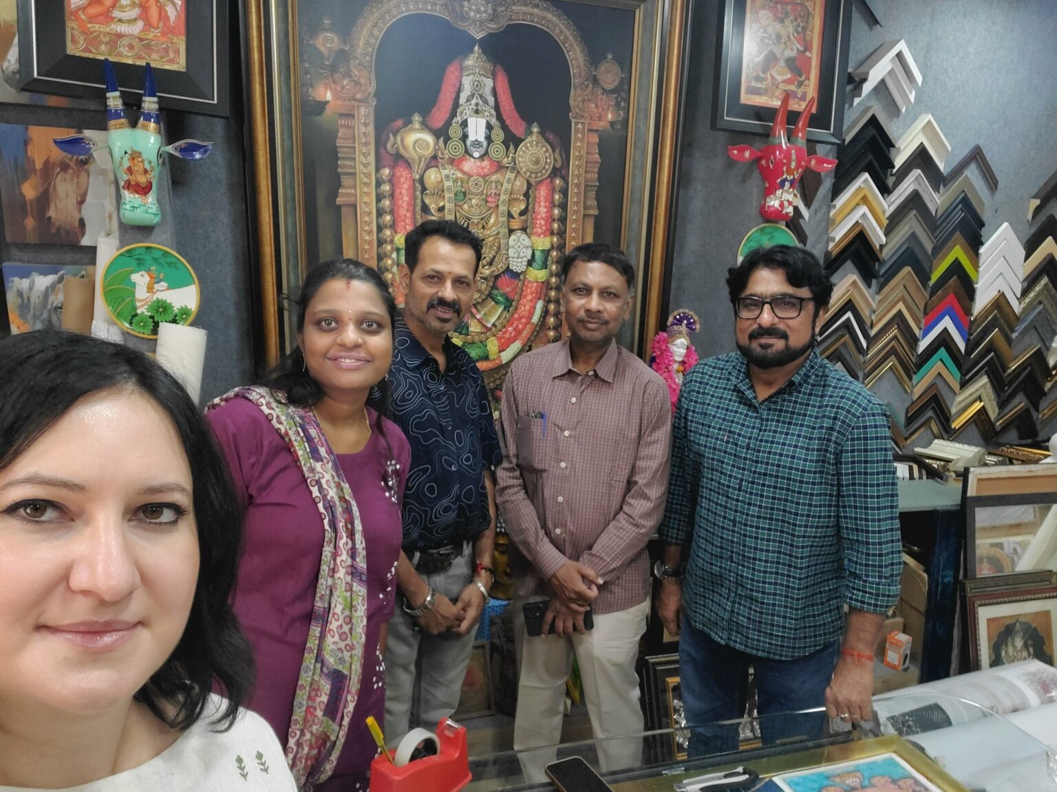 Pięć osób, w tym kobieta robiąca selfie, stoi w pracowni oprawy obrazów. W tle widoczny jest duży, oprawiony w ramę obraz i ramy.