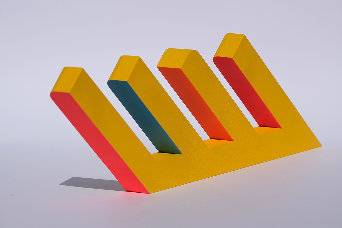 Przedmiot przypominający figurę niemożliwą w kształcie litery "E". Elementy w kolorze żółtym, niektóre boki są różowe, a jeden jest niebieski.