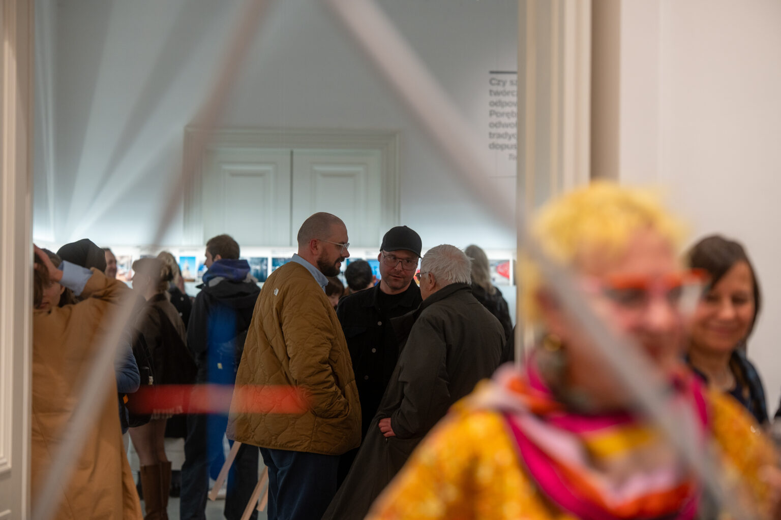 Goście rozmawiający w galerii sztuki, widok przez elementy rzeźby.