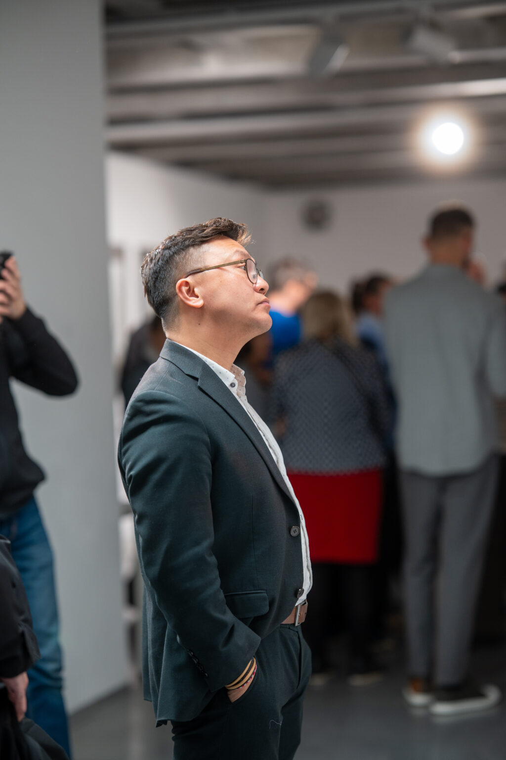 Mężczyzna w ciemnym garniturze i okularach na wystawie w galerii.