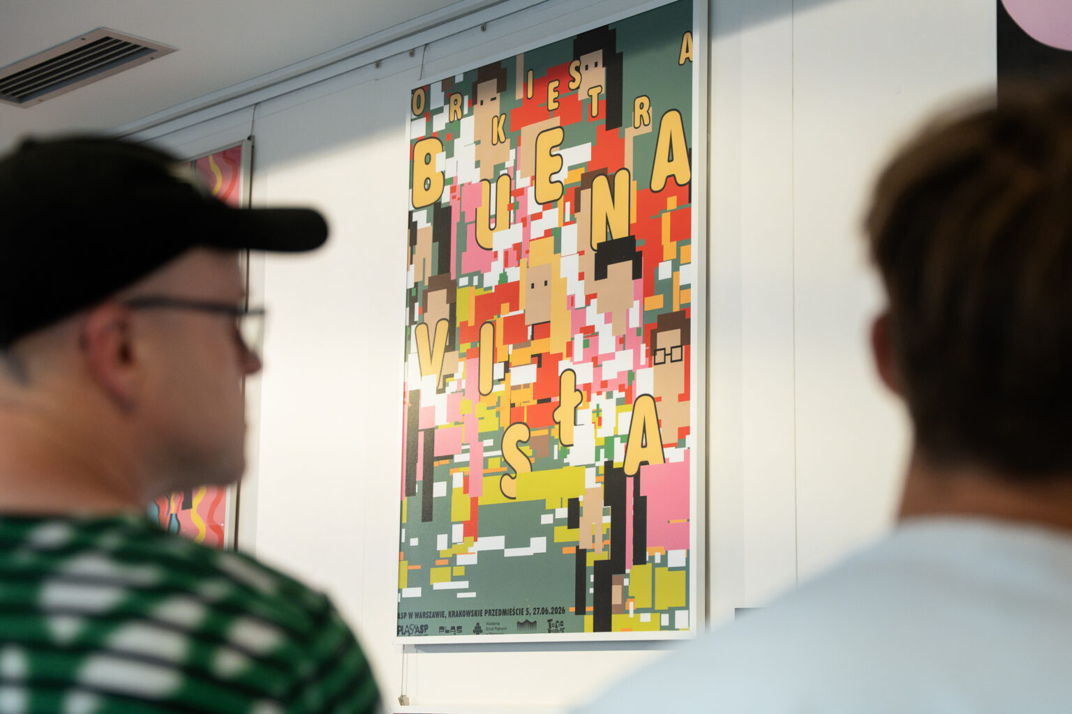 Dwie osoby oglądają plakat przedstawiający napis „Orkiestra Buena Vista”.